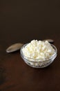 Cottage cheese crumbly in a glass bowl and spoon on a wooden old brown tabletop Royalty Free Stock Photo