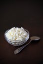 Cottage cheese crumbly in a glass transparent bowl and metal spoon on a wooden old scratched brown tabletop Royalty Free Stock Photo