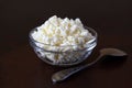 Cottage cheese crumbly in a glass transparent bowl and metal spoon on a wooden old scratched brown tabletop Royalty Free Stock Photo