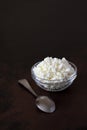 Cottage cheese crumbly in a glass transparent bowl and metal spoon on a wooden old scratched brown tabletop Royalty Free Stock Photo