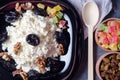 Cottage cheese and prunes on a black plate. Candied fruits, raisins in a wooden box. There is a wooden spoon nearby