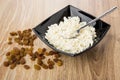 Cottage cheese and teaspoon in black bowl, heap of raisins