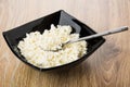 Cottage cheese and teaspoon in black bowl on table