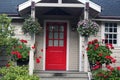 Cottage red door with geraniums and other flower baskets on front porch