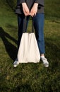 Cotton bag in women`s hands, against the background of green grass in the park. The concept of recycling and