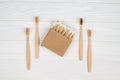 Cotton buds in kraft paper box and natural bamboo toothbrushes on white wooden background - zero waste bathroom essentials.