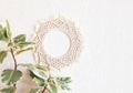 Cotton macrame mandala wall decoration hanging on white wall with green leaves. Handmade macrame wreath. Natural cotton thread.