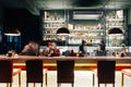 Counter bar with many brands of liquor on glowing shelf with moving bartenders