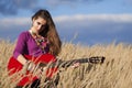 Country girl playing an acoustic guitar in field against blue cloudy sky background Royalty Free Stock Photo