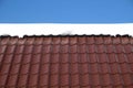 Country house roof from brown metal tile with snow in sunny spring day under blue sky Royalty Free Stock Photo