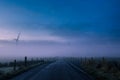 A country lane heading into the distance as three wind turbines rise out the mist on a foggy morning Royalty Free Stock Photo