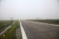 Country road bordered by fields and a channel with an abandoned house in the distance on a foggy day in winter Royalty Free Stock Photo