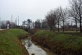 Country road bordered by a stream of water that leads to a railroad crossing on a cloudy day Royalty Free Stock Photo