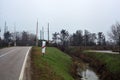 Country road bordered by a stream of water that leads to a railroad crossing on a cloudy day Royalty Free Stock Photo