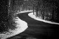 A country road curves uphill surrounded by snow in winter, black and white Royalty Free Stock Photo