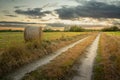 Country road and hay bale in the field, evening view with clouds Royalty Free Stock Photo