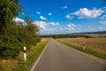 Country road next to a field, and trees along the way with a blue sky and small white clouds Royalty Free Stock Photo