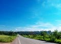 Country road rolls over hills and through a thick forest. Blue sky,
