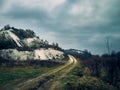 A country road winds between chalk mountains, trees and grass, cloudy sky, late autumn evening Royalty Free Stock Photo