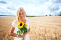 Countryside beauty. Positive young woman standing in a wheat field and holding some sunflowers. Royalty Free Stock Photo