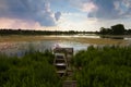 Countryside landscape with heavy rain clouds in the sky and little shabby worn wooden fishing boat at a lake bank footbridge