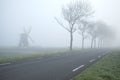 Countryside road by windmill on foggy morning