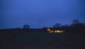 Countryside winter landscape with illuminated house at dusk.