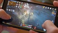 A man holds a smartphone and plays Korean MMORPG Black Desert Online on it, close-up video,