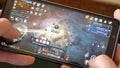A man holds a smartphone and plays MMORPG Black Desert Online, close-up video, illustrative