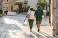 A couple of adult man and woman walk down the street a woman holds medical mask in her hand, a man has mask on his elbow