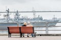 Couple of aged tourists admire view on seaport with warships of Russian Pacific Fleet in city downtown. Russia, Vladivostok