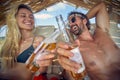 Couple at beach laying on sunbeds cheering with beer. Young man and woman on summer holiday together. Vacation, fun, lifestyle Royalty Free Stock Photo