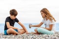 Couple of beautiful teens, first love. Girlfriend and boyfriend sitting on the beach and playing with pebble stones