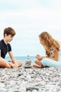 Couple of beautiful teens, first love. Girlfriend and boyfriend sitting on the beach and playing with pebble stones