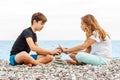 Couple of beautiful teens, first love. Girlfriend and boyfriend sitting on the beach and playing with pebble stones