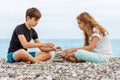 Couple of beautiful teens, first love. Girlfriend and boyfriend sitting on the beach and playing with pebble stones Royalty Free Stock Photo