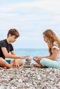 Couple of beautiful teens, first love. Girlfriend and boyfriend sitting on the beach and playing with pebble stones