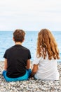 Couple of beautiful teens, first love. Guy hugs a girl sitting on the pebble beach next to each other and looking at the sea.