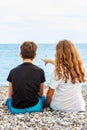 Couple of beautiful teens, first love. Guy hugs a girl sitting on the pebble beach next to each other and looking at the sea.