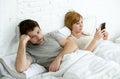 Couple in bed husband frustrated upset and unsatisfied while his internet addict wife is using mobile phone Royalty Free Stock Photo