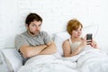 Couple in bed husband frustrated upset and unsatisfied while his internet addict wife is using mobile phone Royalty Free Stock Photo