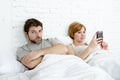 Couple in bed husband frustrated upset and unsatisfied while his internet addict wife is using mobile phone Royalty Free Stock Photo