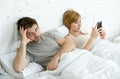 Couple in bed husband frustrated upset unsatisfied while wife using mobile phone Royalty Free Stock Photo