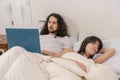 Couple in bed. The man entertaining with the laptop while the woman sleeps Royalty Free Stock Photo
