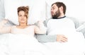 Man snoring and woman can`t sleep, covering ears with pillow for snore noise