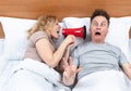 Couple in bed, a woman shouts into a red megaphone at a man who wakes up with fright in his eyes. Snoring as a problem