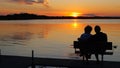 A couple on a bench on a dock enjoy a sunset over a beautiful lake Royalty Free Stock Photo