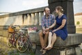 Couple with bicycles sitting on a stone embankment. Love.