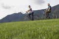 Couple Biking On Grass Against Mountain Range Royalty Free Stock Photo