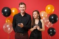 Couple in black clothes messaging in cellphone celebrating birthday holiday party isolated on red background air Royalty Free Stock Photo